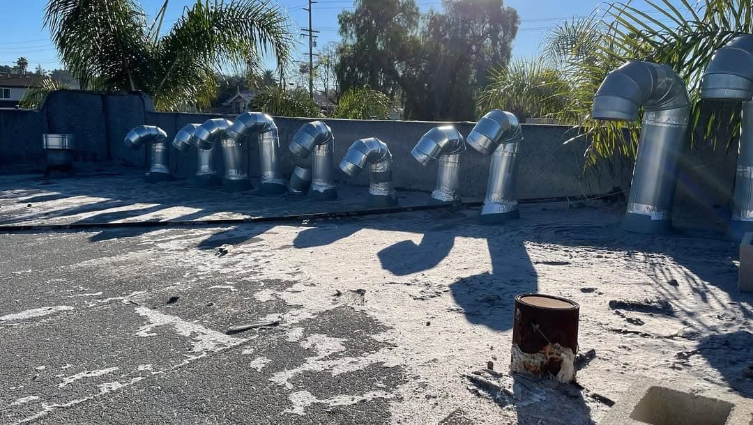 Roof with multiple metal ducts and pipes surrounded by palm trees and clear blue skies.