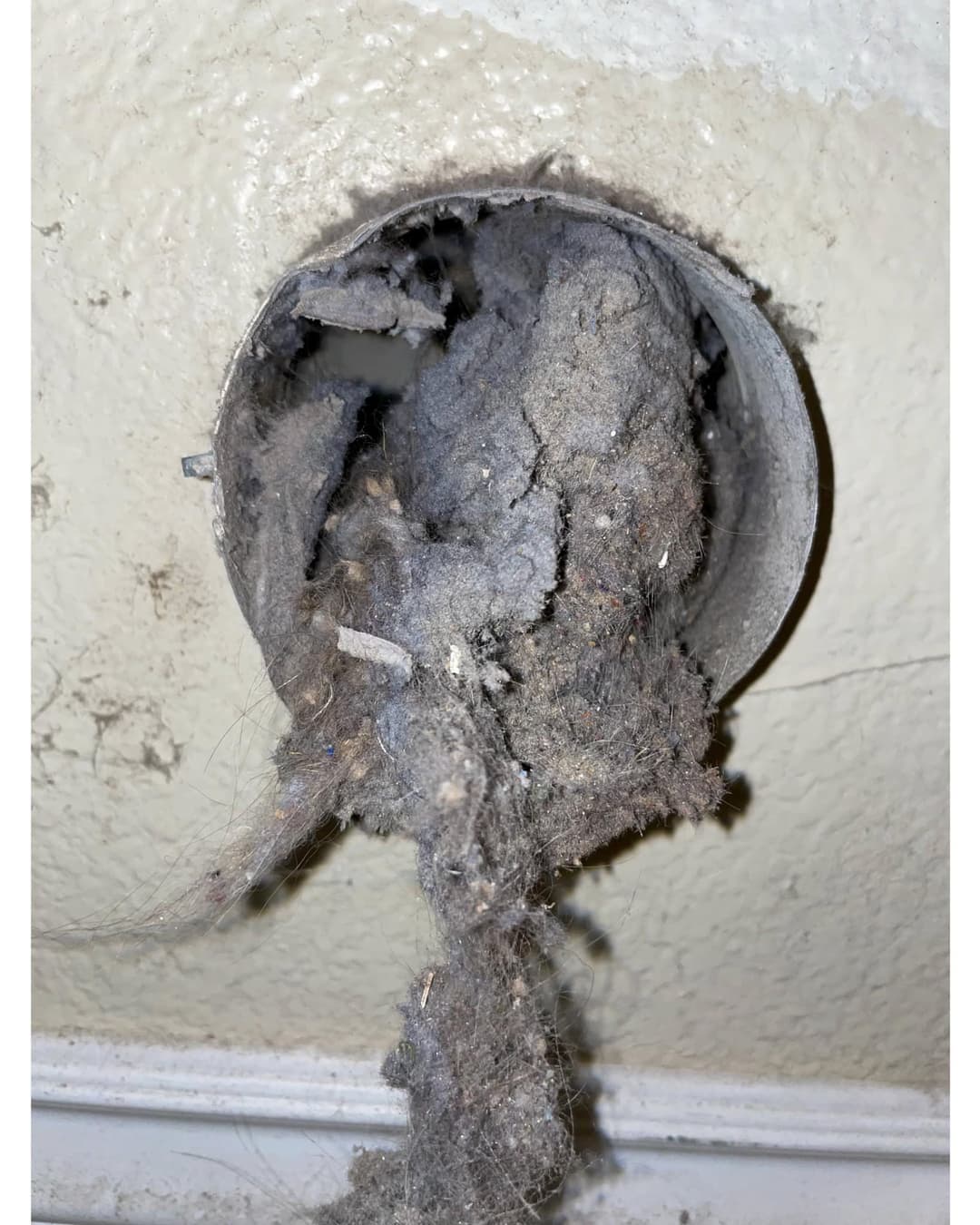 Clogged dryer vent with lint buildup on wall vent, posing fire hazard and reduced airflow.