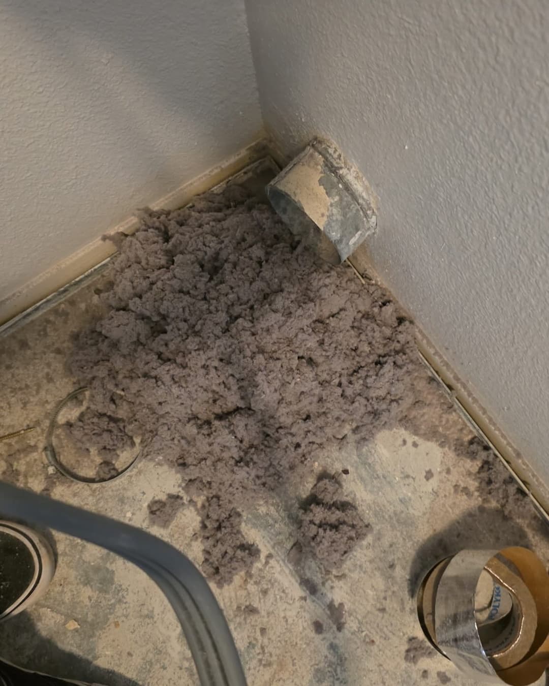 Accumulation of lint and debris near a vent pipe in a residential laundry area.
