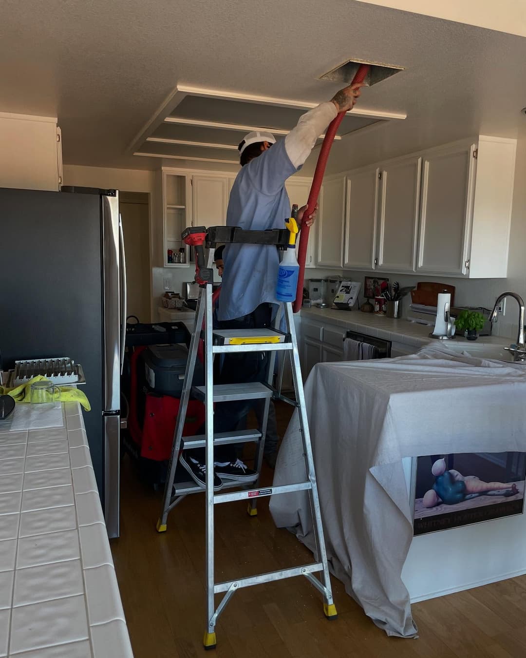 Person using a vacuum attachment while standing on a ladder in a modern kitchen renovation.
