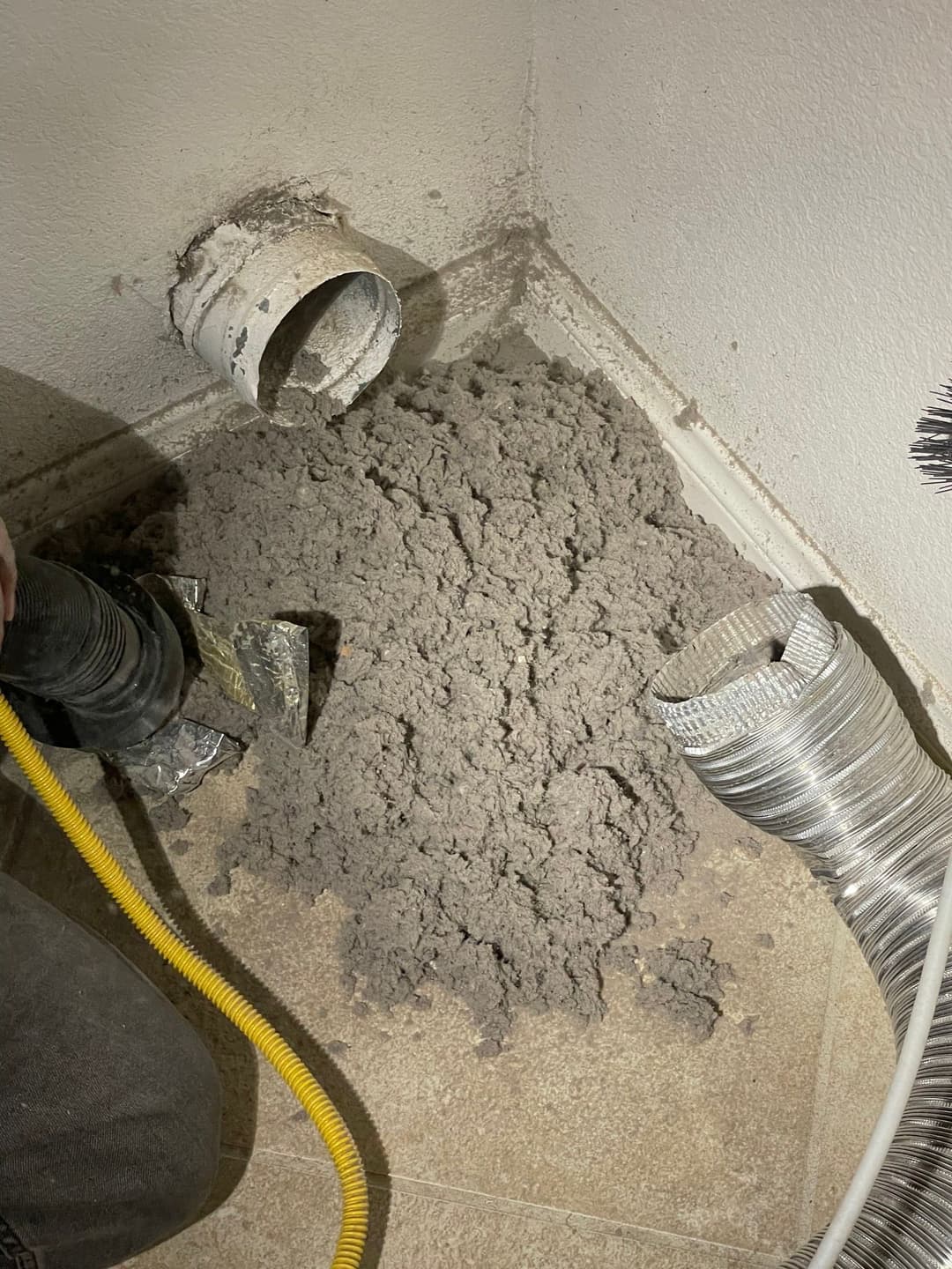 Dryer vent cleaning showing lint buildup near vent and ductwork in corner of a room.